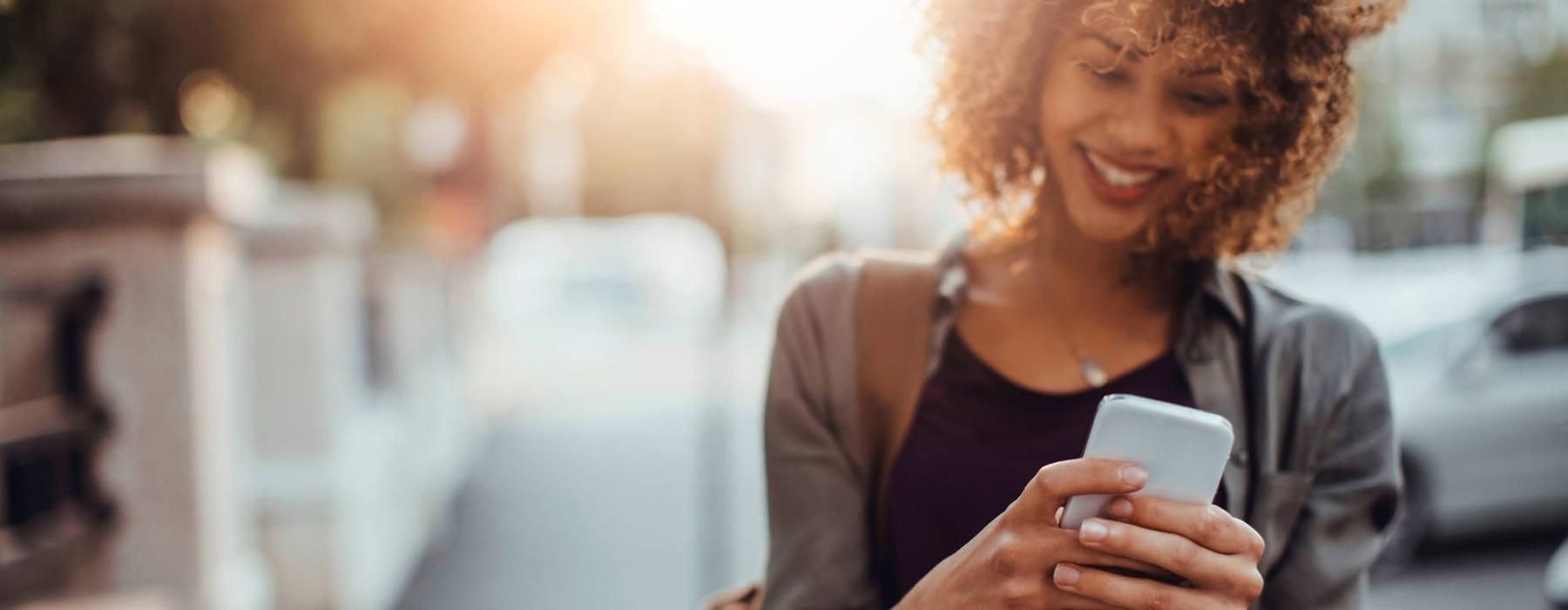 woman texts on her phone as she walks through the city