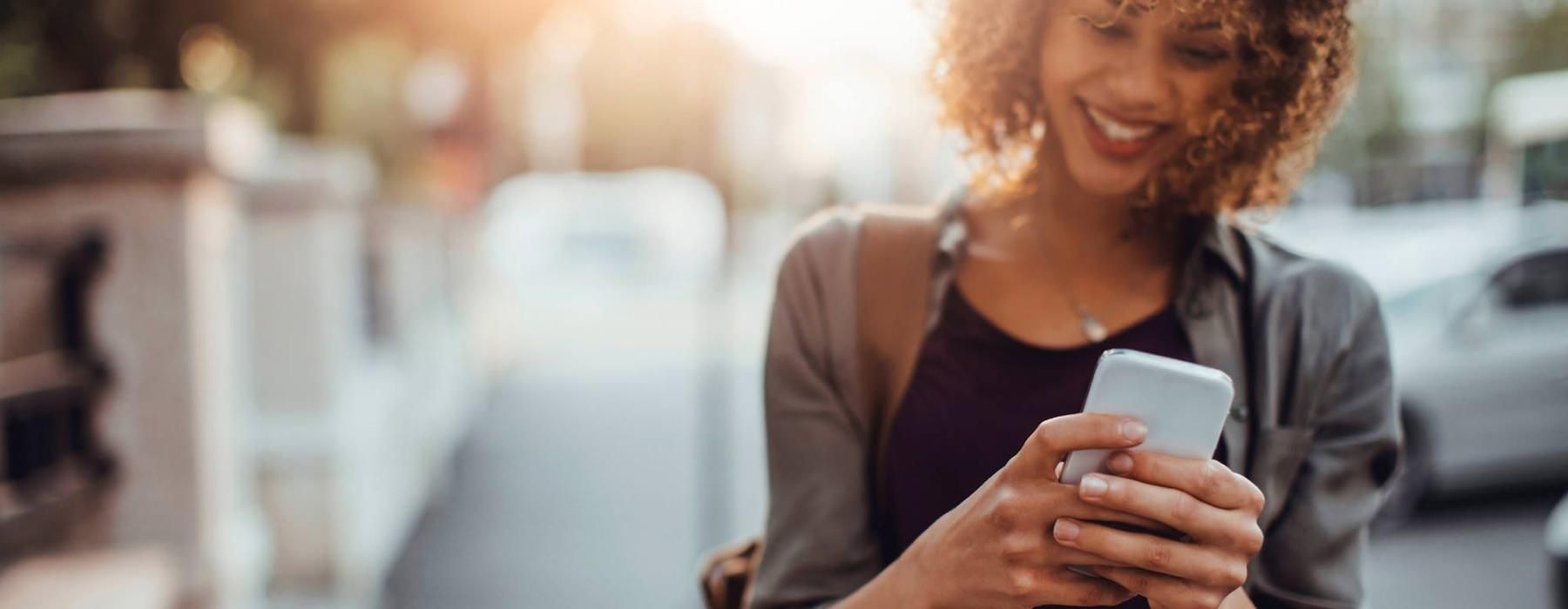 woman texts on her phone as she walks through the city